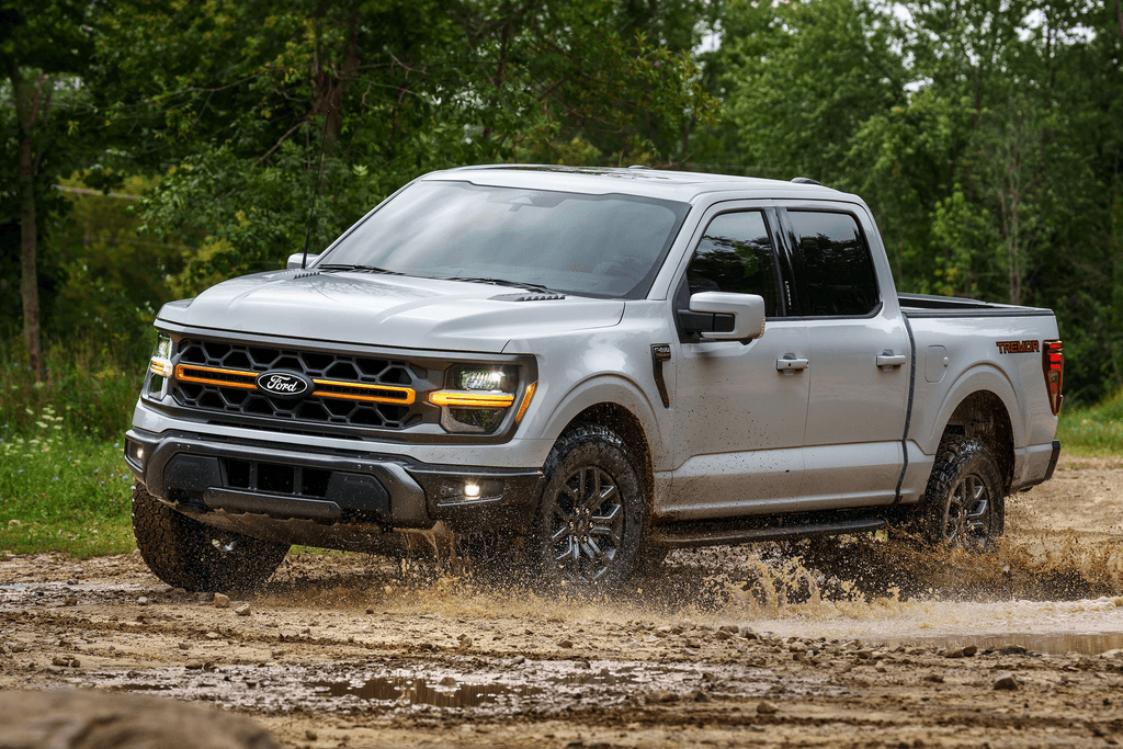 2025 Ford F-150 Tremor driving through mud on a wooded trail with the amber grille lit