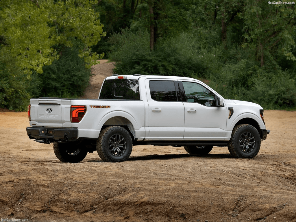 2025 Ford F-150 Tremor rear three-quarter view in white on a dirt trail showing the lifted stance and 33-inch tires