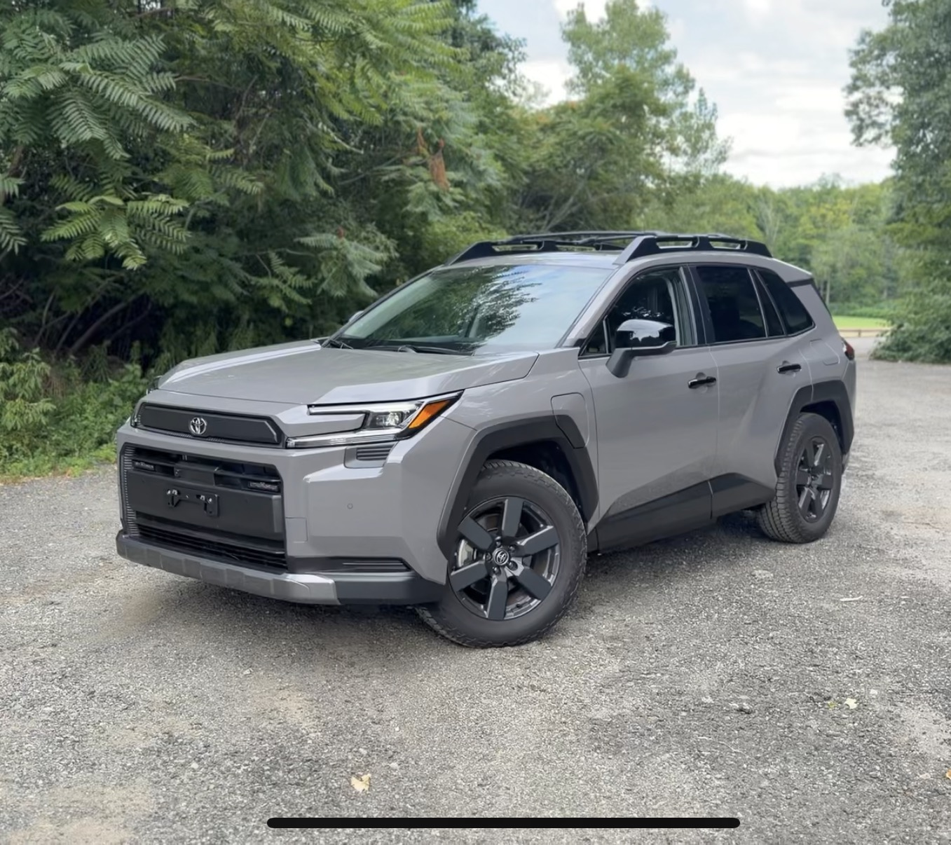 2026 Toyota RAV4 Woodland parked on a gravel road in Urban Rock gray with the charge door visible