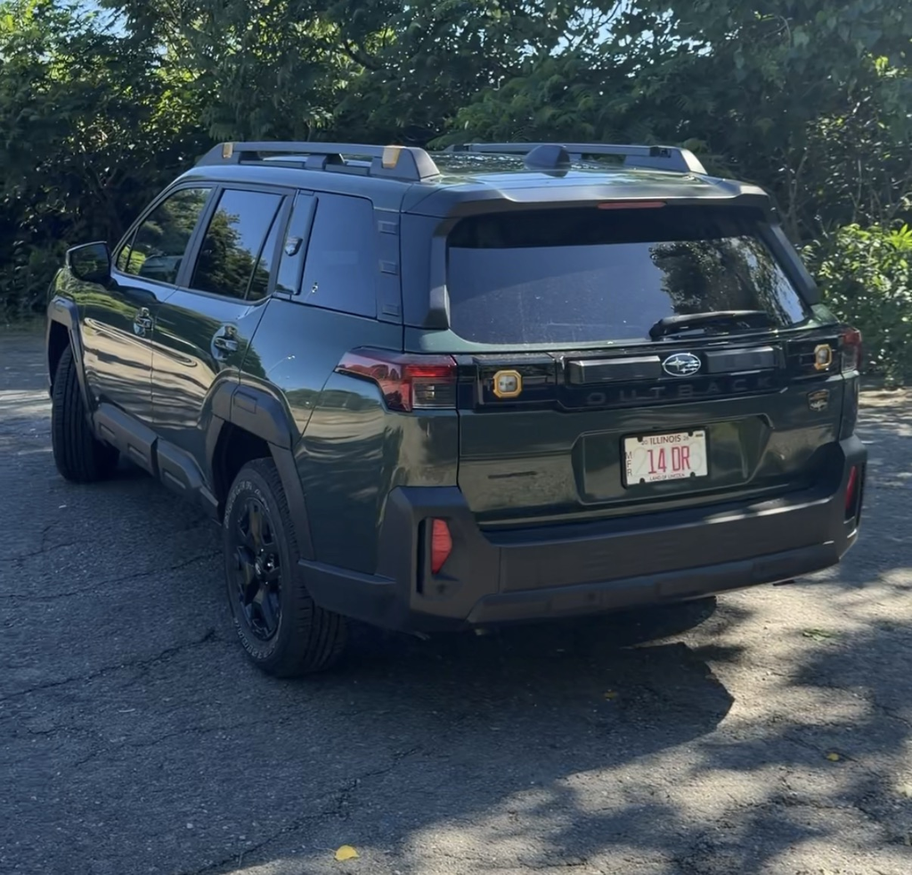 2026 Subaru Outback Wilderness rear three-quarter view in Deep Emerald Green Pearl showing the upright tailgate and roof rails