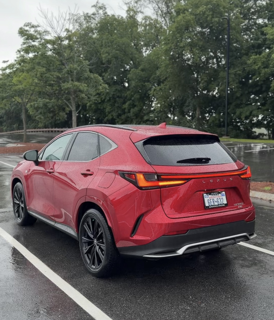 2026 Lexus NX 350h rear three-quarter view in red showing the full-width taillight bar in the rain