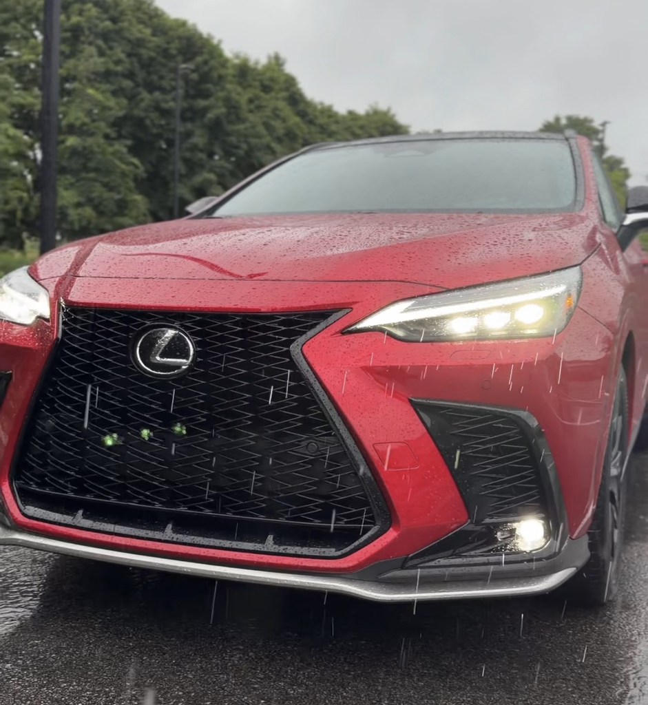 Front grille and headlight detail of the 2026 Lexus NX 350h F Sport in red with rain falling