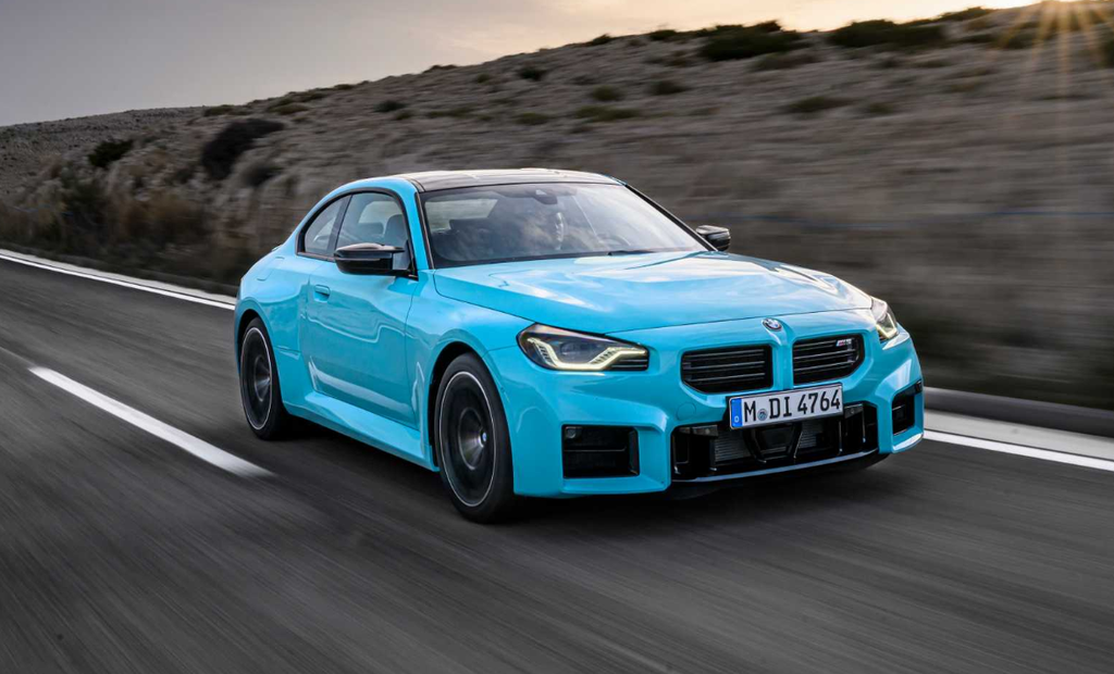 BMW M2 in Zandvoort Blue driving on a mountain road at sunset, front three-quarter view