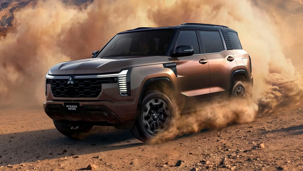 2027 Mitsubishi Pajero front three-quarter view in bronze kicking up desert dust with T-shaped LED headlights lit