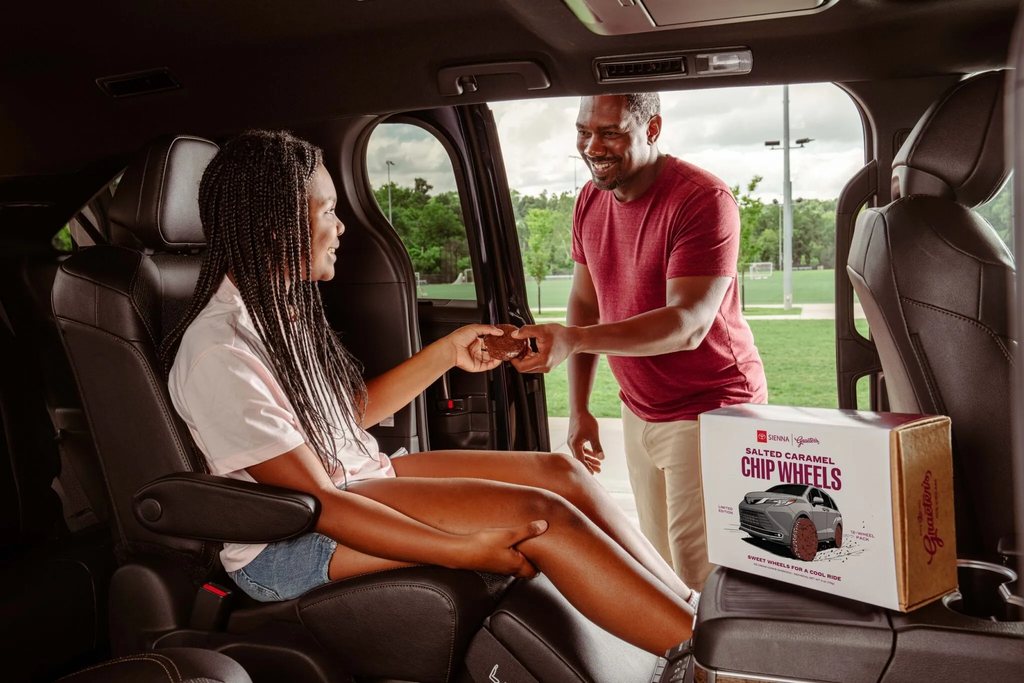 Father handing a Chip Wheels ice cream sandwich to his daughter in the second row of a Toyota Sienna with the box on the console