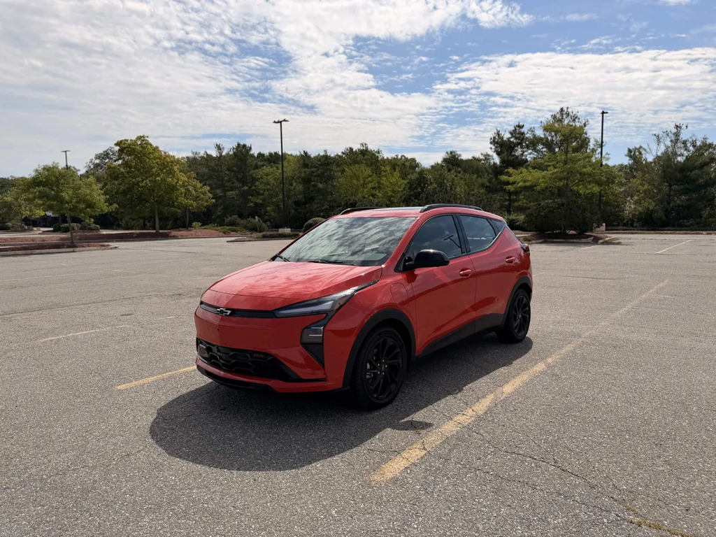 2027 Chevrolet Bolt RS front three-quarter view in red with black wheels in an empty parking lot