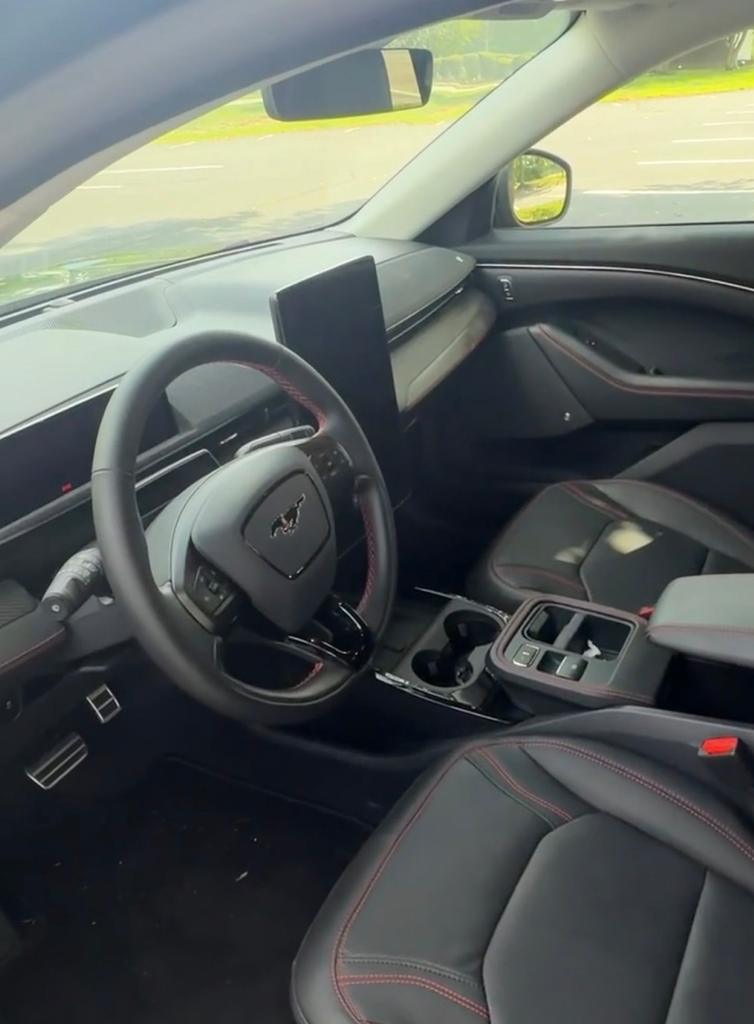 2026 Ford Mustang Mach-E interior showing the vertical touchscreen, digital cluster, and red-stitched seats