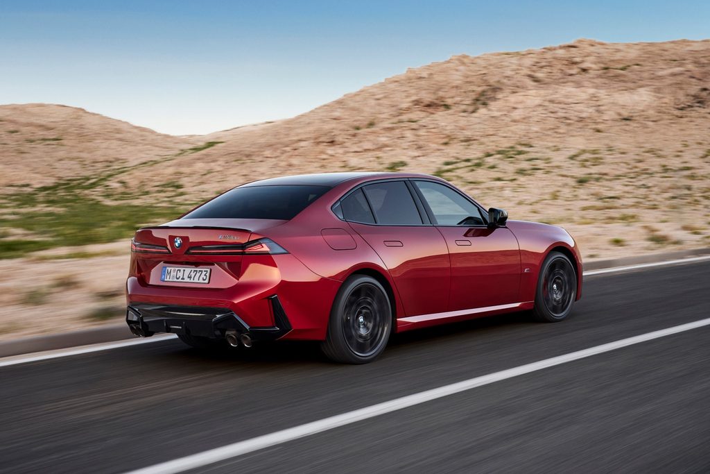 Red BMW M350 xDrive driving on a mountain road, rear three-quarter view